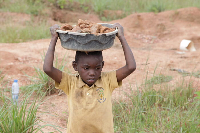 Ein Junge trägt eine Schale mit Steinen auf seinem Kopf (Quelle: Christian Herrmanny) Ein Junge trägt eine Schale mit Steinen auf seinem Kopf (Quelle: Christian Herrmanny)